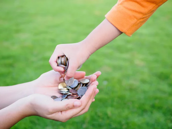 abstract money saving for family. kid hand is holding coins to put on or give to mother hands that holding another coins with green grass background