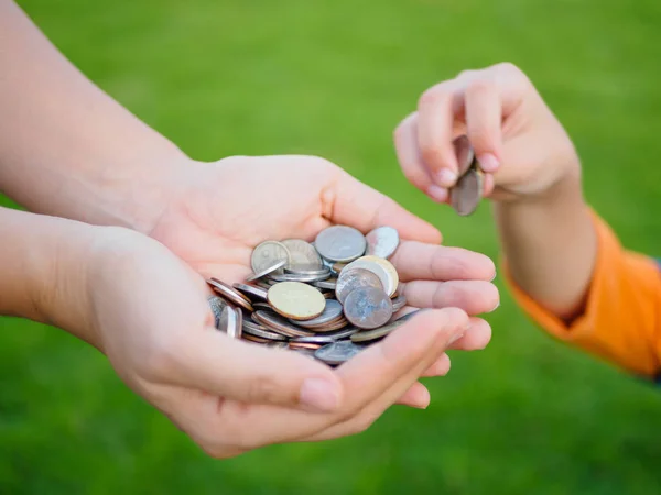 Abstract money saving for family. kid hand is holding coins to put on or give to mother hands that holding another coins with green grass background — Stock Photo, Image