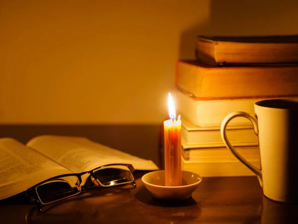 Zásobník staré potrhané knihy na dřevěný stůl, zapálil svíčku a brýle — Stock fotografie