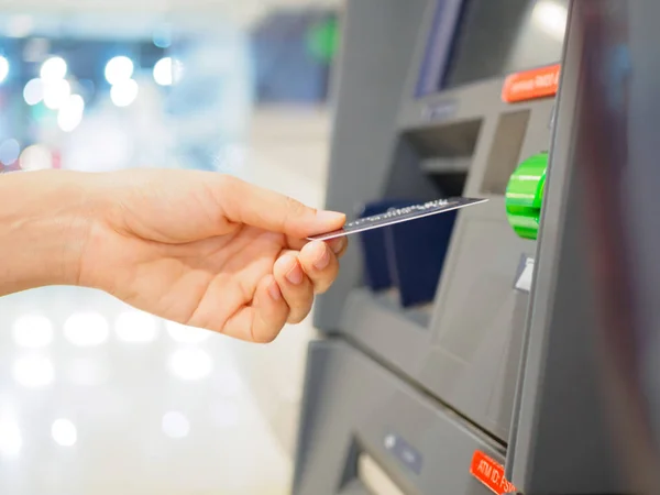 Close-up of woman's hand inserting debit card into an ATM machine. Horizontal shot.