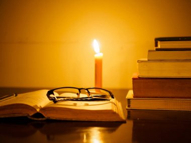 eski püskü kitap yığını ile açılan kitap hakkında bir ahşap masa ışıklı mum ve gözlük