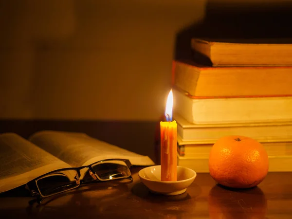 Opened book with stack of old tattered book on a wooden table lighted candle and glasses — Stock Photo, Image