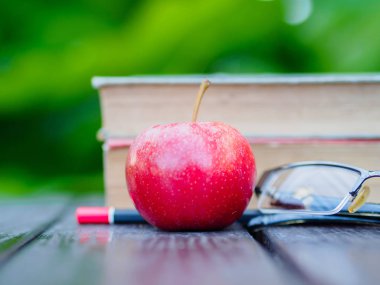 Kitap, kalem, gözlük ve ahşap masa üzerinde kırmızı elma yığını