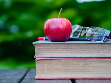 Kitap, kalem, gözlük ve ahşap masa üzerinde kırmızı elma yığını