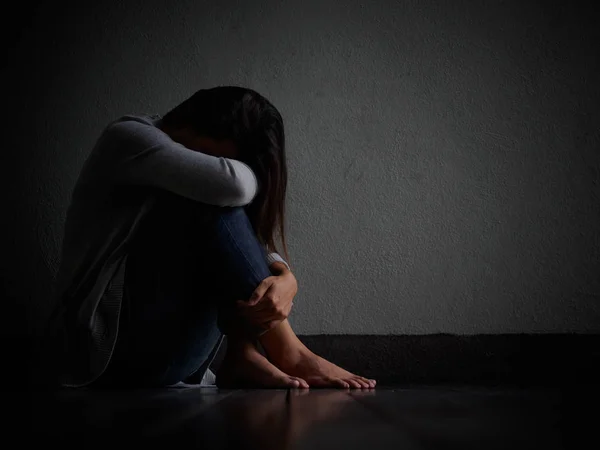 Sorgliga kvinnan krama henne knä och gråta. Sorgliga kvinna sitter ensam i ett tomt rum. — Stockfoto