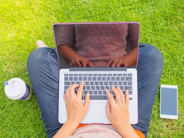 Dizüstü bilgisayar kullanan genç ve güzel kadın. Bir açık yeşil çim sahası içinde laptop üzerinde erkek