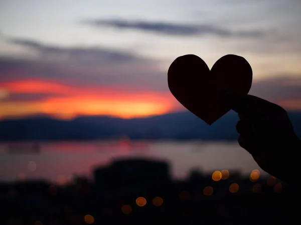 Silhouette Hand hebt das rote Papierherz mit verschwommenem Sonnenlicht während Sonnenuntergang, Valentinstag — Stockfoto