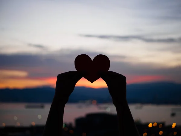 Silhouette Hand hebt das rote Papierherz mit verschwommenem Sonnenlicht während Sonnenuntergang, Valentinstag — Stockfoto