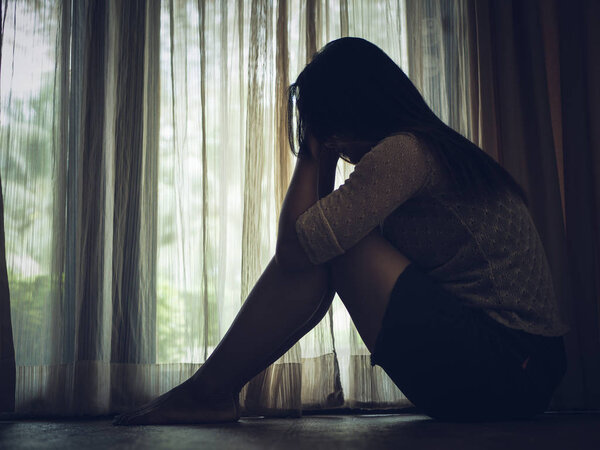 black and white of sad woman hug her knee and cry. Sad woman sitting alone in a empty room beside window or door