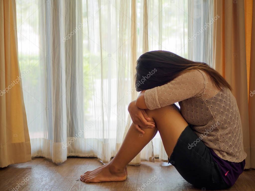 black and white of sad woman hug her knee and cry. Sad woman sitting alone in a empty room beside window or door