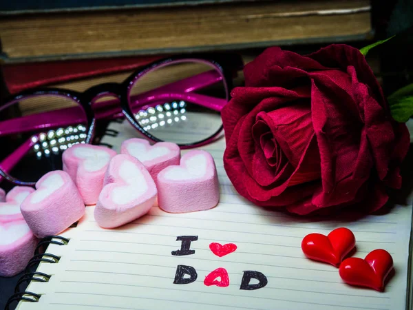 Conceito de dia do pai. I LOVE DAD message write on note book with red rose, pilha de livros, óculos e doce marshmallow na forma de coração no fundo escuro — Fotografia de Stock