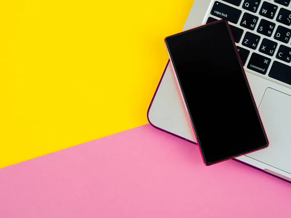 Bovenaanzicht van smartphone op laptop op roze en gele achtergrond — Stockfoto