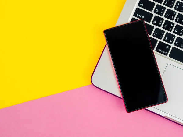 Bovenaanzicht van smartphone op laptop op roze en gele achtergrond — Stockfoto