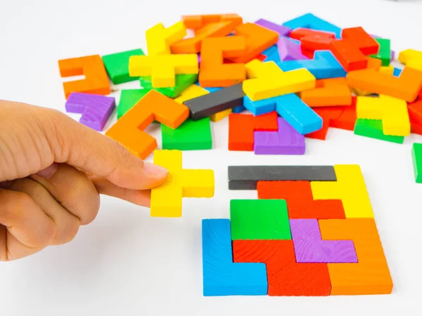 Hand hält das letzte Teil, um ein quadratisches Tangram-Puzzle zu vervollständigen buntes Holzpuzzle für Kinder auf weißem Hintergrund — Stockfoto