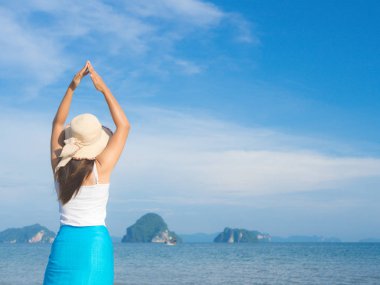 Yaz tatilindeki kadın hasır şapka ve plaj elbisesi giyip okyanus manzarasının tadını çıkarıyor.