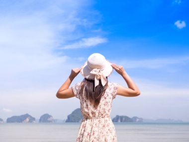 Hasır şapka ve okyanus manzaraya bakarak plaj elbisesi giyen yaz tatili yalnız kadın