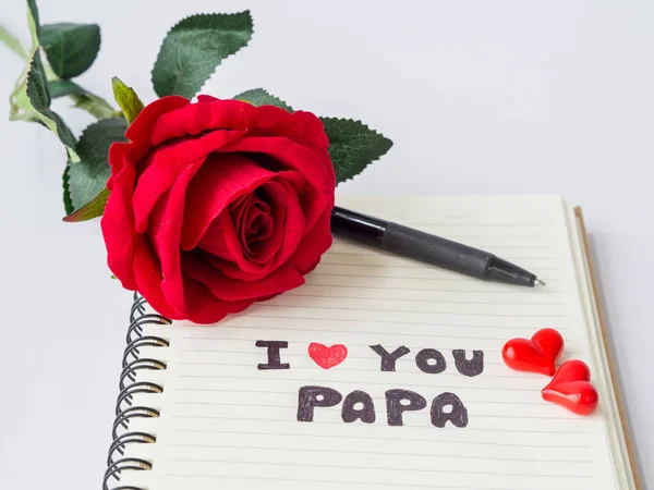 Concepto del día del padre. Me encanta el mensaje de PAPA escribir en el libro de notas con rosa roja, gafas y dos corazones rojos sobre fondo blanco — Foto de Stock