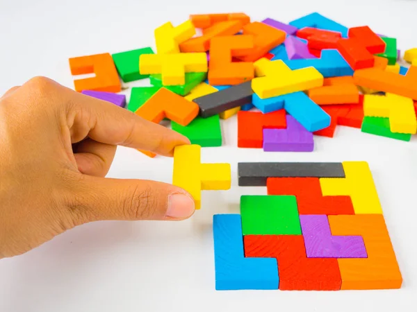 Ruka držící poslední kousek k dokončení čtvercové tangram puzzle barevné dřevěné puzzle pro děti na bílém pozadí — Stock fotografie