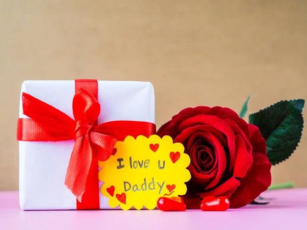 Concepto del día del padre. TE AMO Mensaje de papá con rosa roja, dos corazones rojos y regalo sobre fondo rosa — Foto de Stock