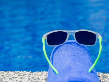 güneş gözlüğü ve havuz kenarındaki mavi havlu. Tatil, plaj, yaz seyahat kavramı