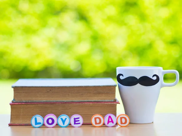 Concepto del día del padre. LOVE papá alfabeto en pila de libros, regalos, taza de té con bigote negro y flor en el fondo — Foto de Stock