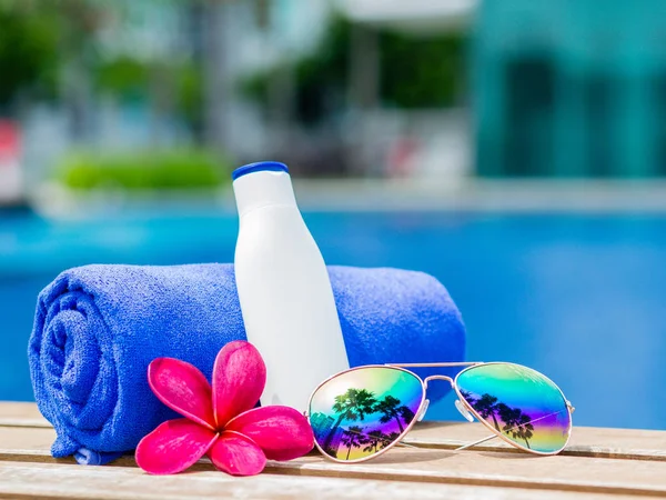 Frangipani rojo (plumeria) flores, gafas de sol, toalla azul y protector solar al lado de la piscina. Vacaciones, playa, concepto de viaje de verano — Foto de Stock