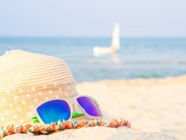 şapka ve güneş gözlüğü deniz ve yelkenli artalanları, yaz seyahat kavramı ile sahilde