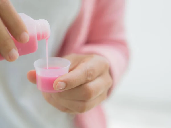 Assistenza sanitaria, persone e concetto di medicina - donna che versa farmaci o sciroppo antipiretico da bottiglia a tazza — Foto Stock