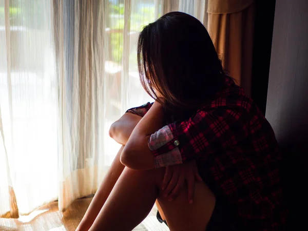 Mujer triste abrazar su rodilla y llorar. Mujer triste sentada sola en una habitación vacía al lado de una ventana o puerta — Foto de Stock