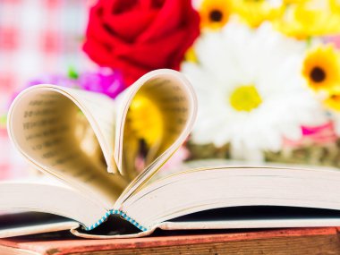 kitap ve backgroung içinde çiçek ile kalp şekli oluşturan sayfaları açıldı. Sevgi ve Sevgililer günü kavramı.