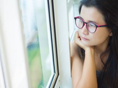 Siyah beyaz tek başına oturmak ve pencereden bakarak üzgün kadın giyim gözlük.