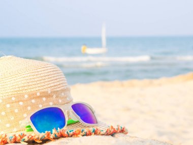 şapka ve güneş gözlüğü deniz ve yelkenli artalanları, yaz seyahat kavramı ile sahilde