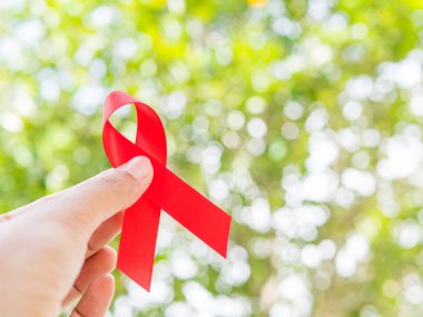 Dünya AIDS günü kavramı. Kırmızı kurdele ağaç üzerinde tutan el bokeh arka plan bırakır.