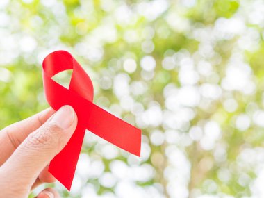 Dünya AIDS günü kavramı. Kırmızı kurdele ağaç üzerinde tutan el bokeh arka plan bırakır.