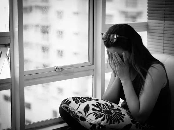 Mujer Mujer deprimida o triste usa gafas sentada sola y cubriéndose la cara debido a tener un dolor de cabeza cerca de la ventana . — Foto de Stock