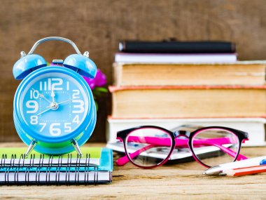 Ofis aksesuarları yığın kitap, hesap makinesi, gözlük, kırmızı kalem, mavi kalem, çalar saat ve ahşap arka plan üzerinde pembe çiçek de dahil olmak üzere. Eğitim ve iş kavramı.