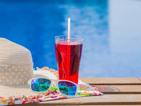 Pastos solares, sombrero, toallas enrolladas y refresco rojo con al lado de la piscina. Vacaciones, playa, concepto de viaje de verano — Foto de Stock