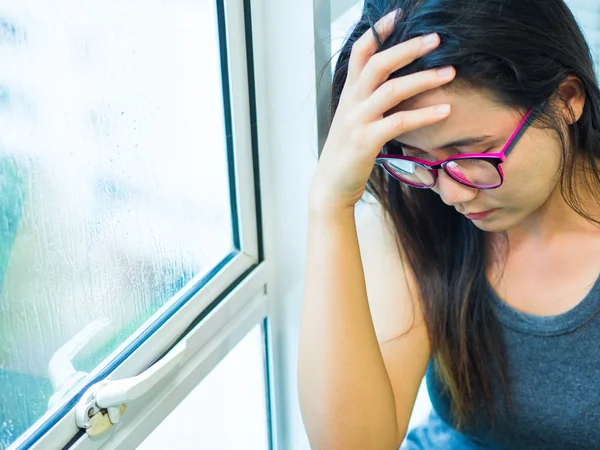 Kvinna Depressed eller ledsen kvinna bära glasögon sitter ensam och täcker hennes ansikte på grund av att ha en huvud värk nära fönstret. — Stockfoto