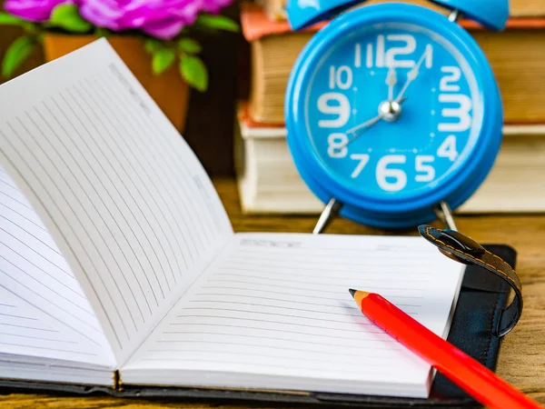 Toebehoren voor kantoor inclusief rode potlood op notitie boek, stapel book, calculator, wekker en roze bloem op houten achtergrond. Onderwijs en bedrijfsleven concept. — Stockfoto