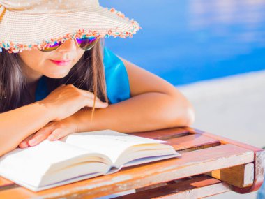 Şezlong üzerinde yalan ve Yüzme Havuzu tarafından bir kitap okuma yaz şapkalı kadın kapatın. Tatil ve dinlenme, yaz seyahat kavramı.