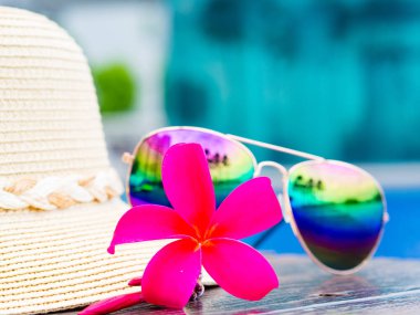 Kırmızı frangipani (plumeria) çiçekler yaz şapka ve güneş gözlüğü havuz kenarında. Tatil ve dinlenme, yaz seyahat kavramı.