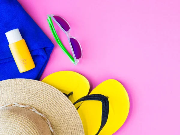 Yaz şapka, flip flop, mavi havlu ve güneş koruyucu losyon pembe bir arka plan üzerinde güneş gözlüğü. Tatil ve dinlenme, yaz seyahat kavramı.
