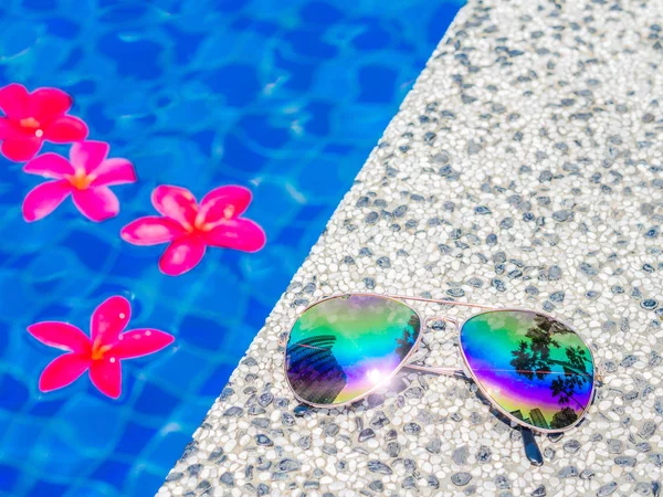 Gafas de sol y flores de frangipani rojo (plumeria) al lado de la piscina. Vacaciones, playa, concepto de viaje de verano — Foto de Stock