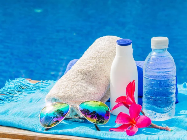 Frangipani rojo (plumeria) flores, gafas de sol, protector solar, toallas azules y blancas al lado de la piscina. Vacaciones, playa, concepto de viaje de verano — Foto de Stock