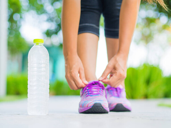 Running shoes - closeup of woman tying shoe laces. Female sport fitness runner getting ready for jogging with water bottle in garden background