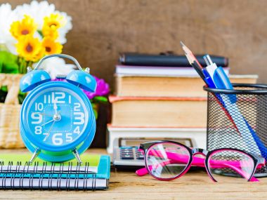 Ofis aksesuarları yığın kitap, hesap makinesi, gözlük, kırmızı kalem, mavi kalem, çalar saat ve ahşap arka plan üzerinde pembe çiçek de dahil olmak üzere. Eğitim ve iş kavramı.