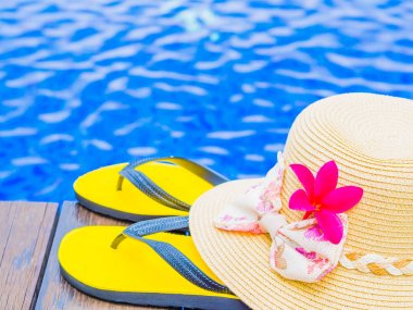 Yaz ile kırmızı frangipani (plumeria) çiçek şapka ve yüzme havuzunun kenarında floplar flip. Tatil ve dinlenme, yaz seyahat kavramı.