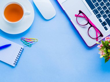 Üstten Görünüm kadınsı Resepsiyon çalışma alanıyla dizüstü bilgisayar, not defteri, mavi kalem, kahve, çiçekler, fare ve mavi arka plan üzerinde pembe gözlük gibi ofis aksesuarları.