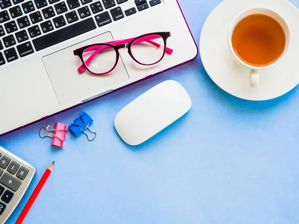 Visão superior espaço de trabalho de mesa feminino com acessórios de escritório, incluindo laptop, café, lápis vermelho, calculadora, clipes, mouse e óculos rosa no fundo azul . — Fotografia de Stock