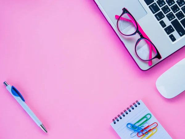 Feminino espaço de trabalho de mesa com acessórios de escritório, incluindo laptop, livro de notas, mouse, clipes e óculos rosa no fundo rosa . — Fotografia de Stock